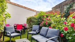 Et udendørs siddeområde med stole og borde, omgivet af frodigt grønt og blomstrende planter.