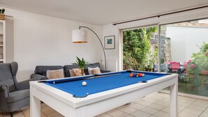 Et billardbord i et rum med en sofa, en lampe og udsigt til en have gennem en glasdør.
