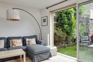 A modern living room with a grey sofa, a small table, and a large window overlooking a garden. - Holiday Home 'In Bordeaux, Air-Conditioned with Pool Table' with Private Terrace and AC (Le Bouscat)