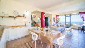 A modern living room with a dining area, a kitchen with white cabinets, and a large window overlooking the sea. - Awesome home in Caronia (Caronia)