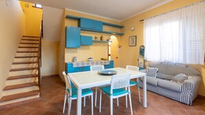 Un coin repas avec une table et des chaises blanches, un buffet bleu et un canapé à rayures.
