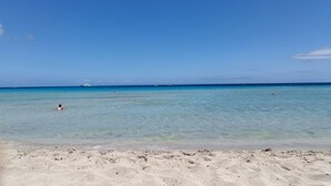 Une plage à l’eau claire, avec un rivage sablonneux et un bateau qui se profile à l’horizon.