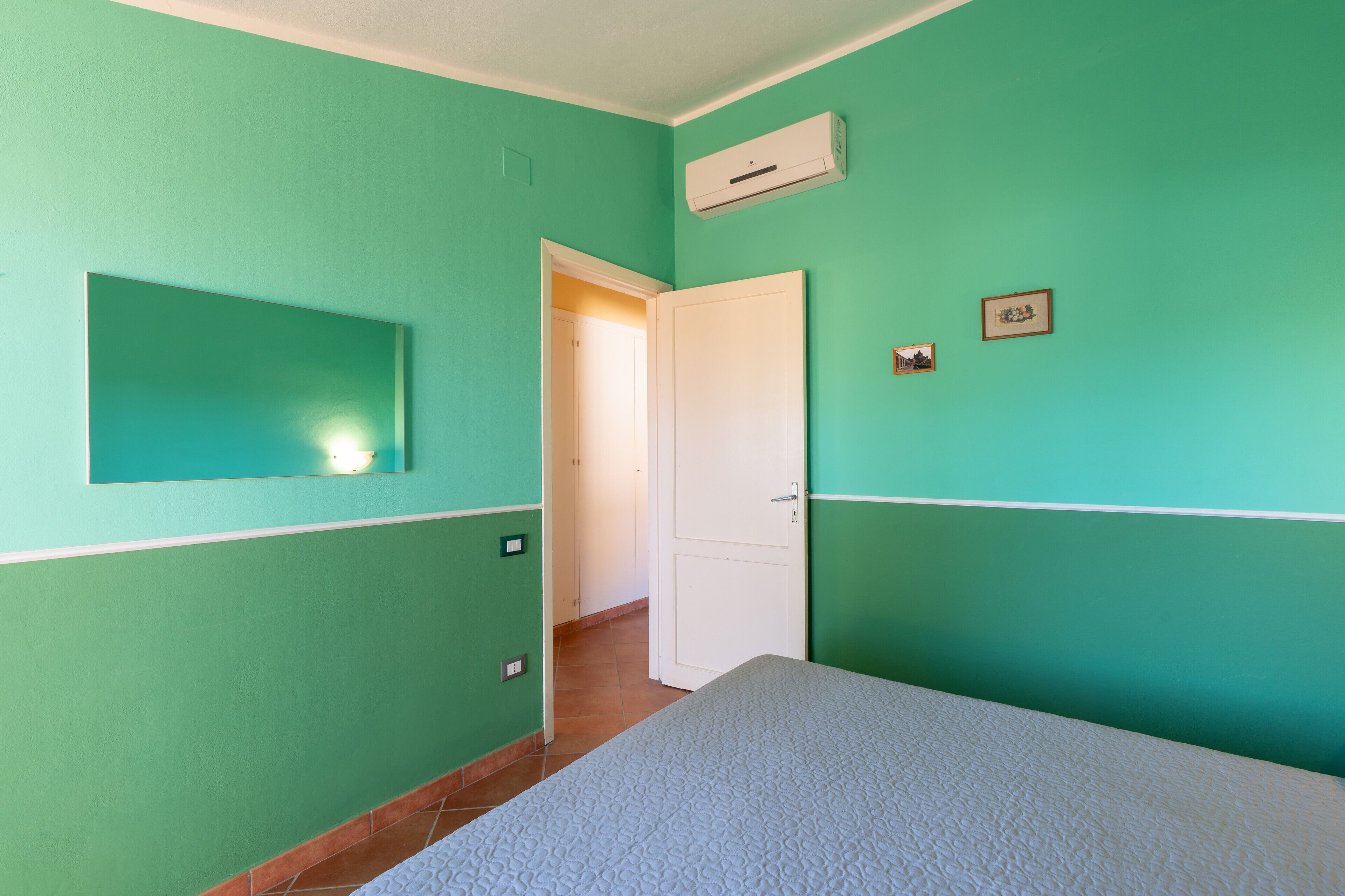 Et værelse med teal vægge, en seng, en dør og en aircondition-enhed.
