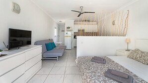 Et moderne hotelværelse med et fladskærms-TV, en sofa, en seng, en ventilator i loftet og et køkkenområde i baggrunden.