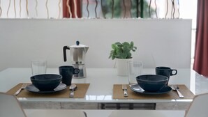 Et spisebord med to sæt skåle, kopper og en kaffemaskine, placeret ved et hvidt bord med udsigt til det fri.