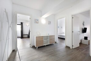 Una habitación moderna y bien iluminada con suelo de madera, un armario blanco y un televisor de pantalla plana sobre una mesita.