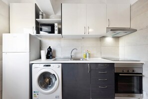 Eine kompakte Küche mit Waschmaschine, Mikrowelle, Backofen und Edelstahlgeräten.