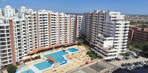 Ein Hochhaus-Hotel mit mehreren Balkonen, einem Pool mit Liegestühlen und Blick auf die umliegende Stadtlandschaft.