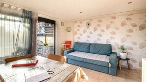 A cozy living room with a blue sofa, a wooden dining table with a red folder, and a potted plant on a small table. - Awesome home in Criquetot-l'Esneval (Criquetot-l'Esneval)
