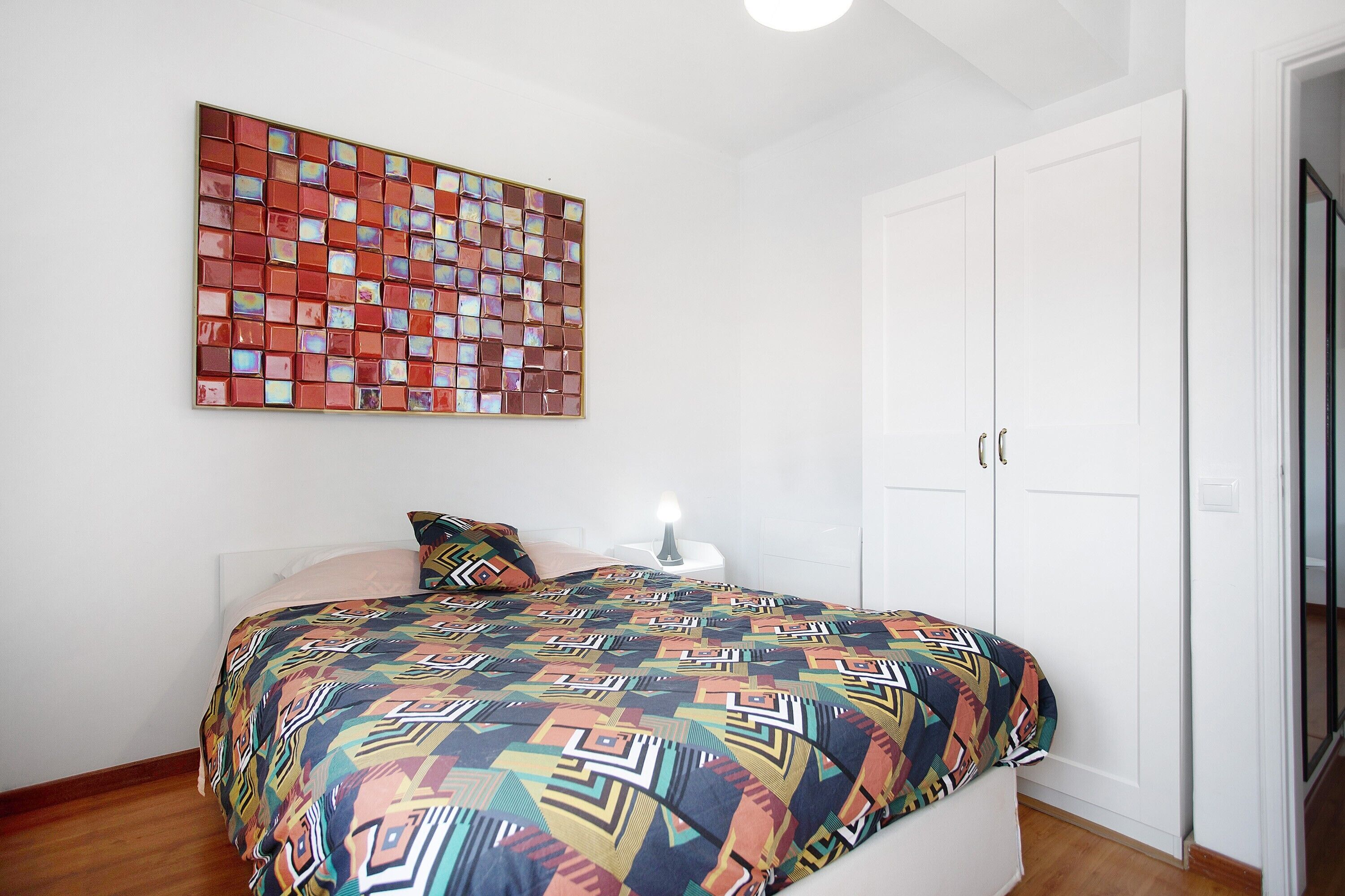 A bedroom with a bed, a wall art piece, a bedside table, and a wardrobe.