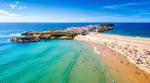 Une plage côtière aux eaux limpides, avec un rivage sablonneux et des bâtiments en arrière-plan.