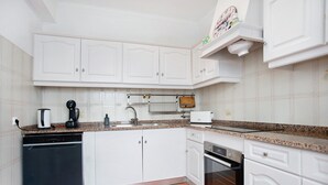 A kitchen with white cabinets, a dishwasher, a coffee maker, a toaster, and an oven. - Apartamento Da Alegria – Feel at Home on the Silver Coast (Caldas da Rainha)