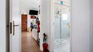 A hallway leading to a bathroom with a glass shower door, a red trash bin, and a wooden floor. - Apartamento Da Alegria – Feel at Home on the Silver Coast (Caldas da Rainha)