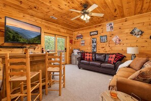 A cabin interior with a wooden interior, a bar area, a sofa, and a television mounted on the wall. - Free Dollywood Tix/Dog Friendly/Gameroom/HotTub/ (Sevierville)