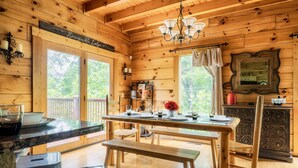 Ein Holzblockhaus-Interieur mit einem für vier Personen gedeckten Esstisch, einer Bank und einer Küchenzeile mit Holzkasten und einer Pendelleuchte.