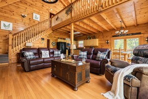 A spacious living room with a wooden staircase, leather sofas, a coffee table, and a dining area. - Free Dollywood Tix/Dog Friendly/Gameroom/HotTub/ (Sevierville)