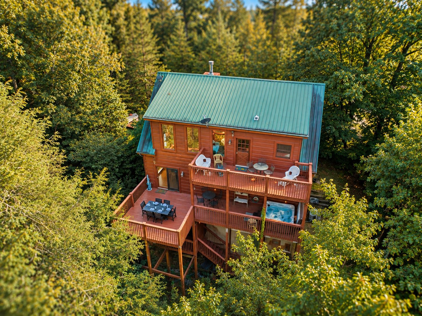A two-story wooden cabin with a green roof, surrounded by dense forest.