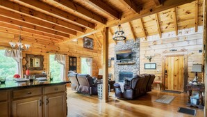 Ein Holzblockhaus im Inneren mit Kamin aus Stein, Ledersofas und einer Küchenzeile.