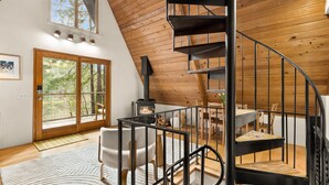 A modern loft with a wooden interior, a spiral staircase, a fireplace, and a large sliding glass door leading to a balcony. - Stylish Lakefront Cabin Retreat, Sauna/Hot tub & Cold Plunge (Gig Harbor)