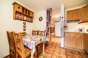 Uma sala de jantar com mesa e cadeiras de madeira, cozinha com armários de madeira e cortina estampada.