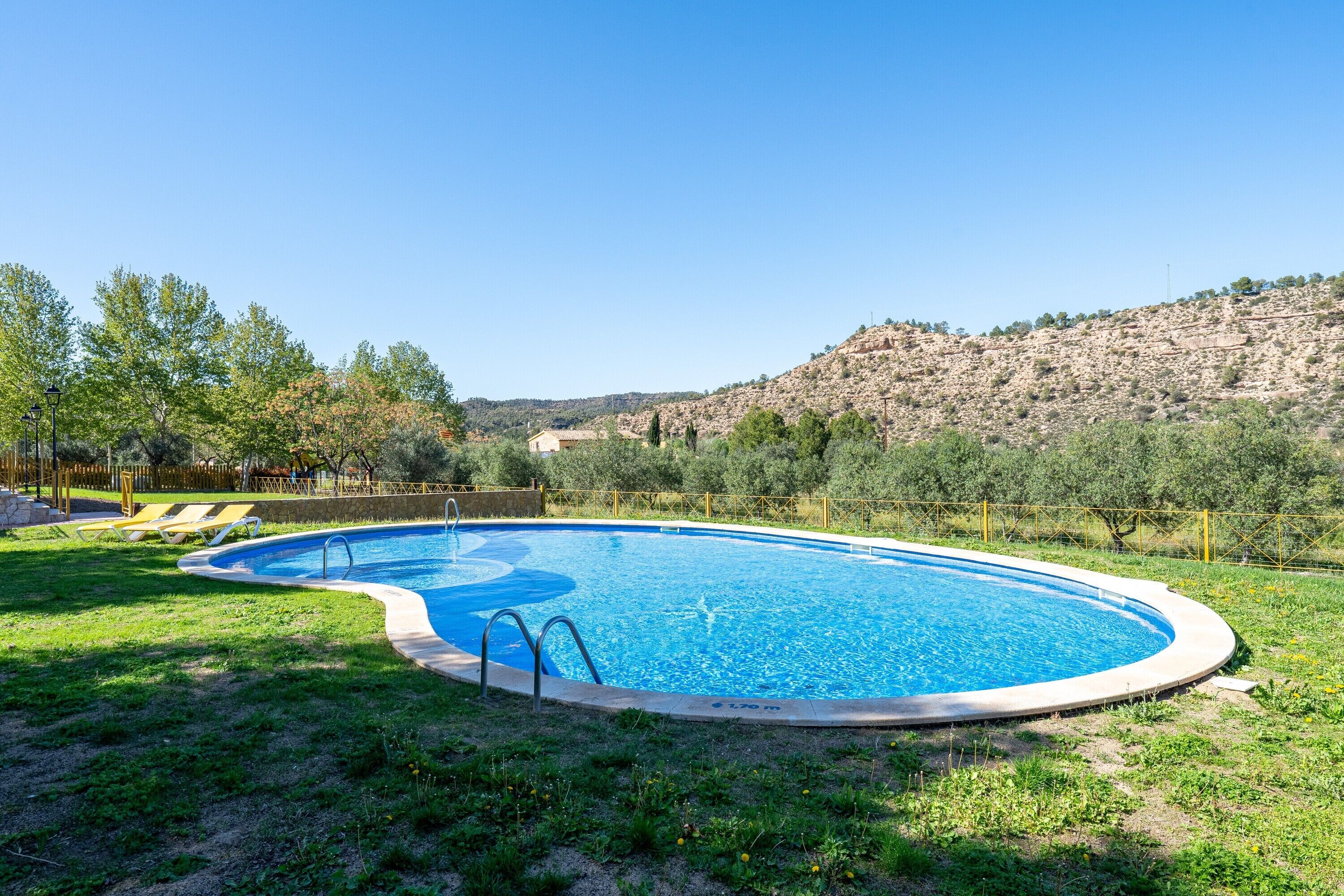 A swimming pool with a grassy area and a fence, surrounded by trees and hills.