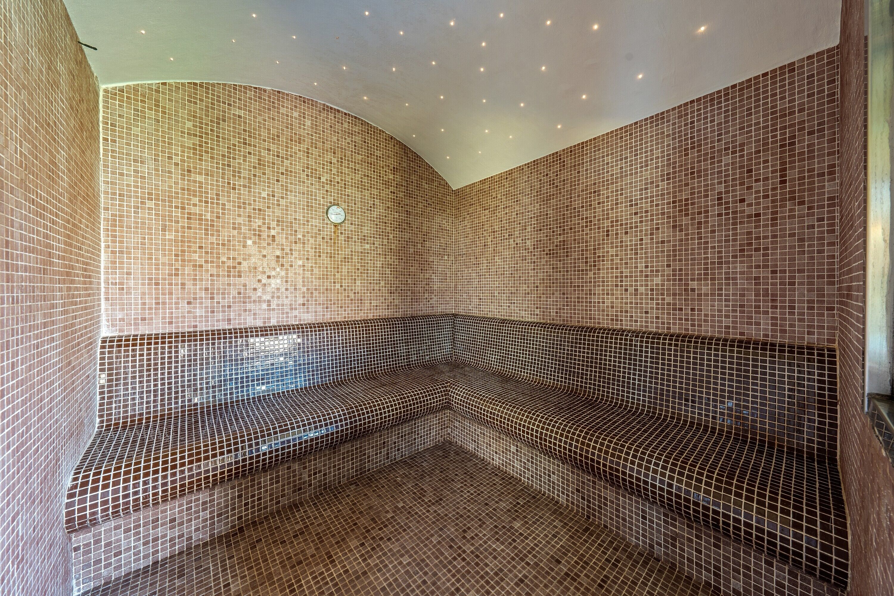 A corner seating area with a tiled wall and ceiling, a clock, and a bench.