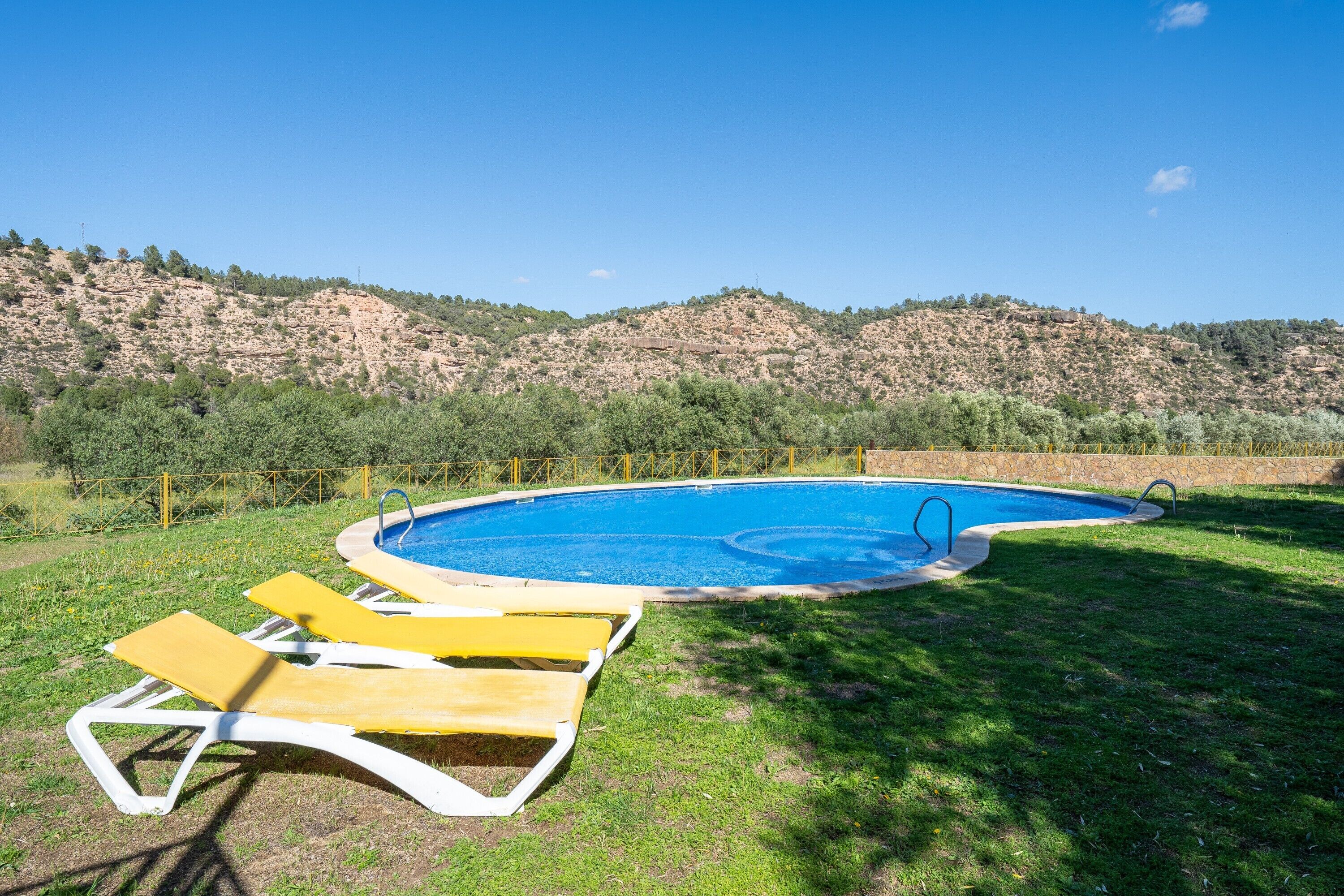 A swimming pool with two yellow lounge chairs and a stone wall in the background.