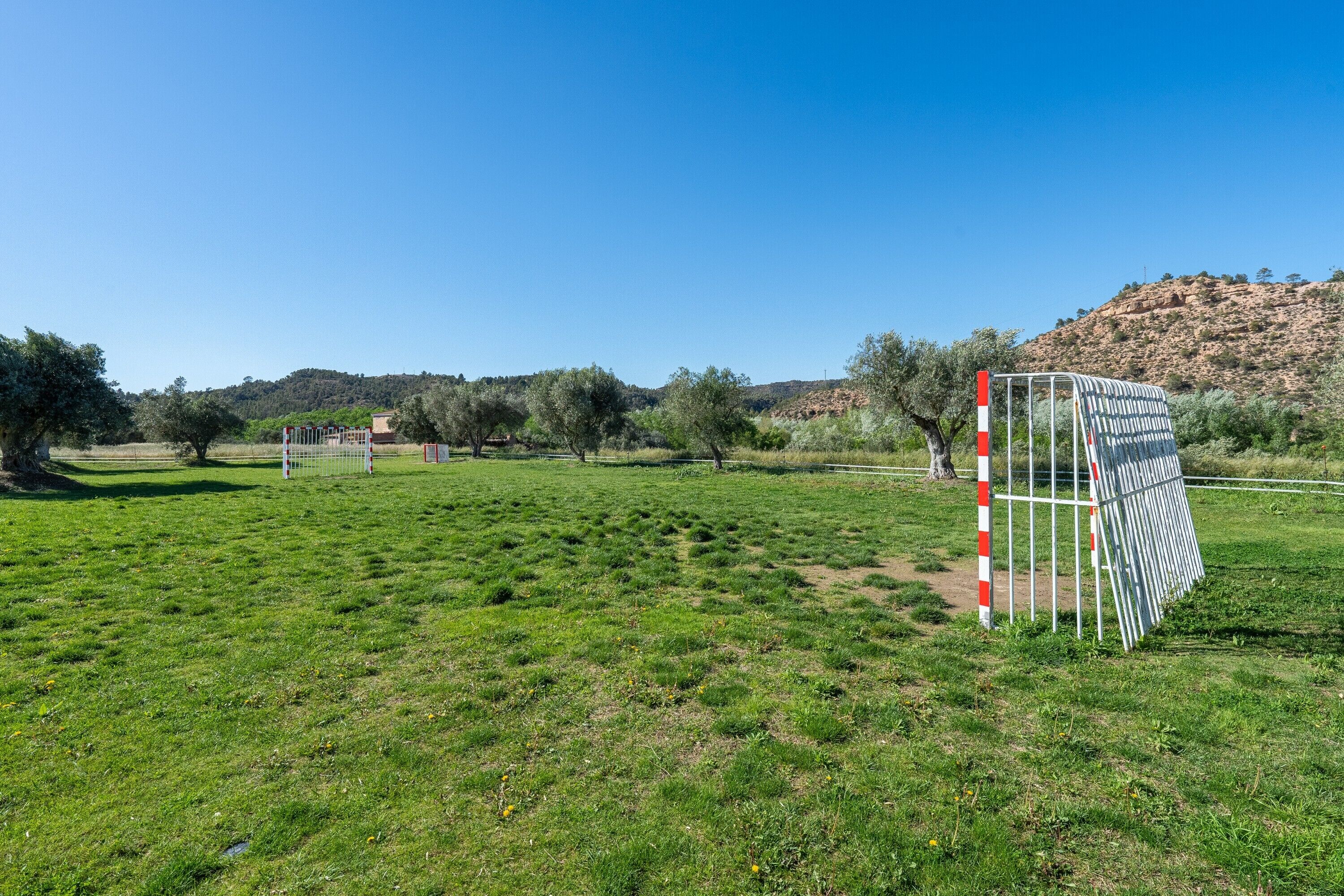 A grassy field with a white and red striped pole, a metal gate, and a hill in the background.