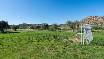 A grassy field with a white and red striped pole, a metal gate, and a hill in the background.