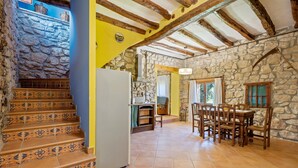 A rustic interior with a stone wall, wooden staircase, tiled floor, and a dining area with wooden furniture.