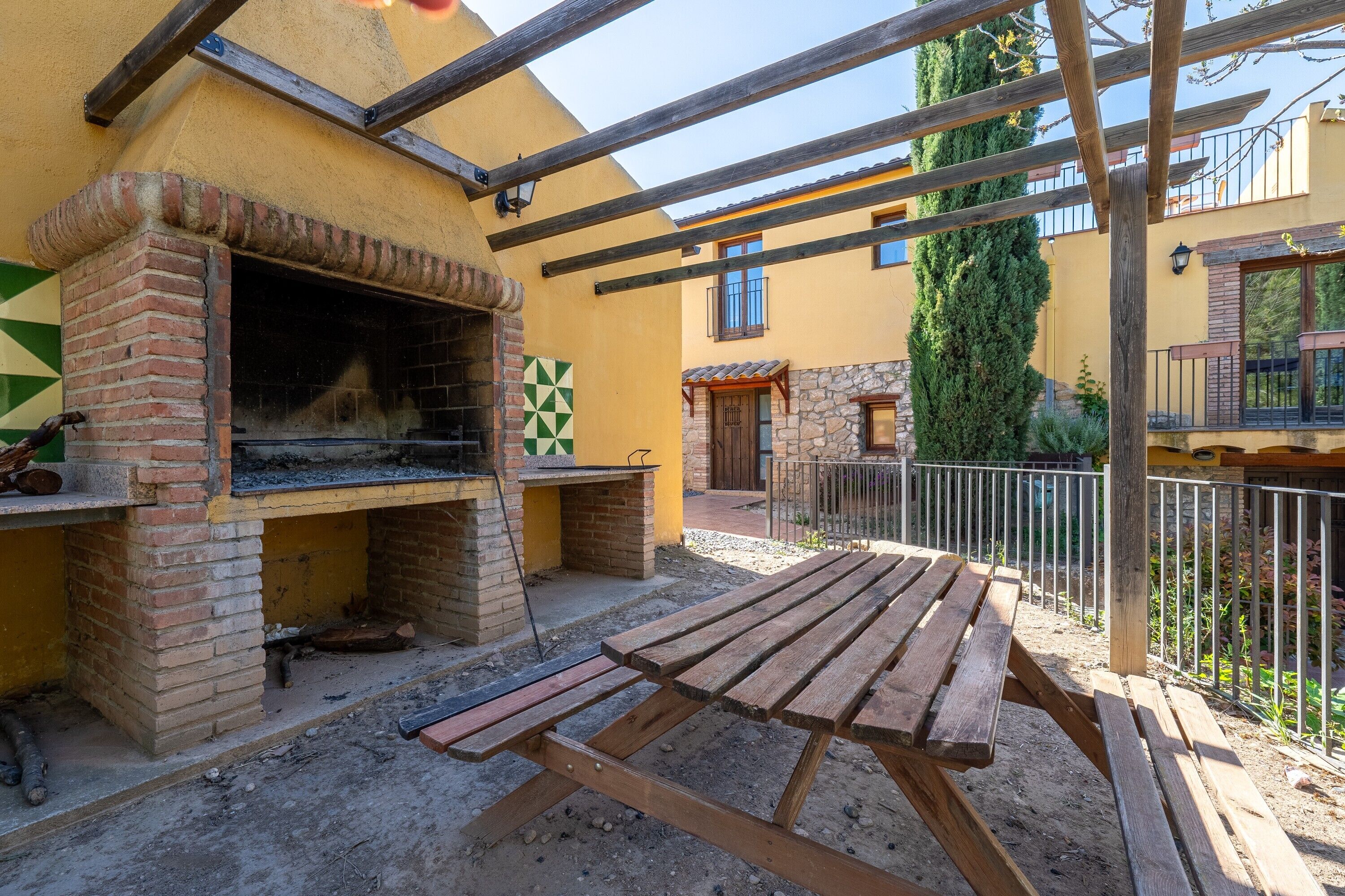 An outdoor patio with a brick oven, wooden table, and a stone wall.