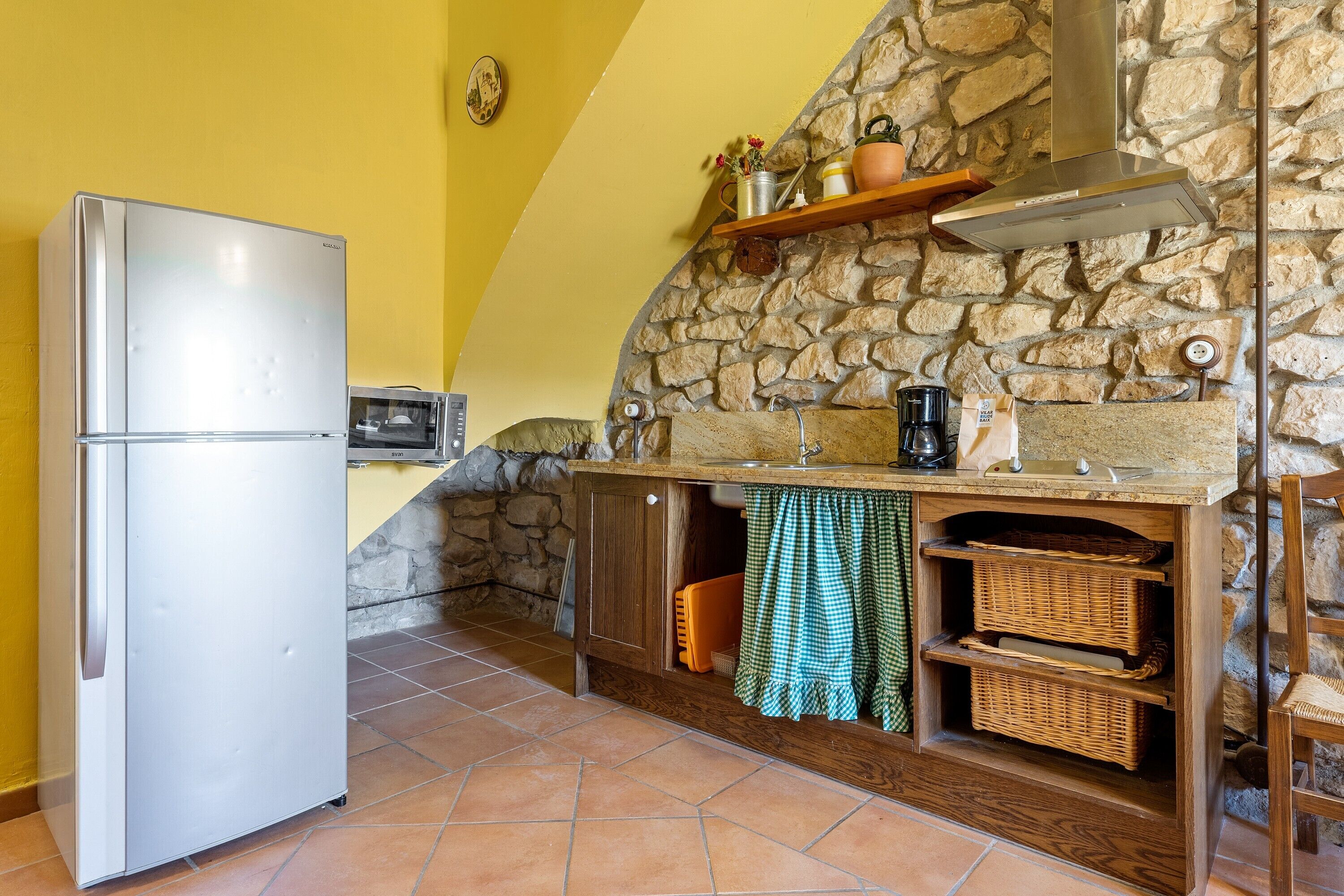 Una cocina con refrigerador blanco, pared de piedra, armarios de madera y encimera de piedra.
