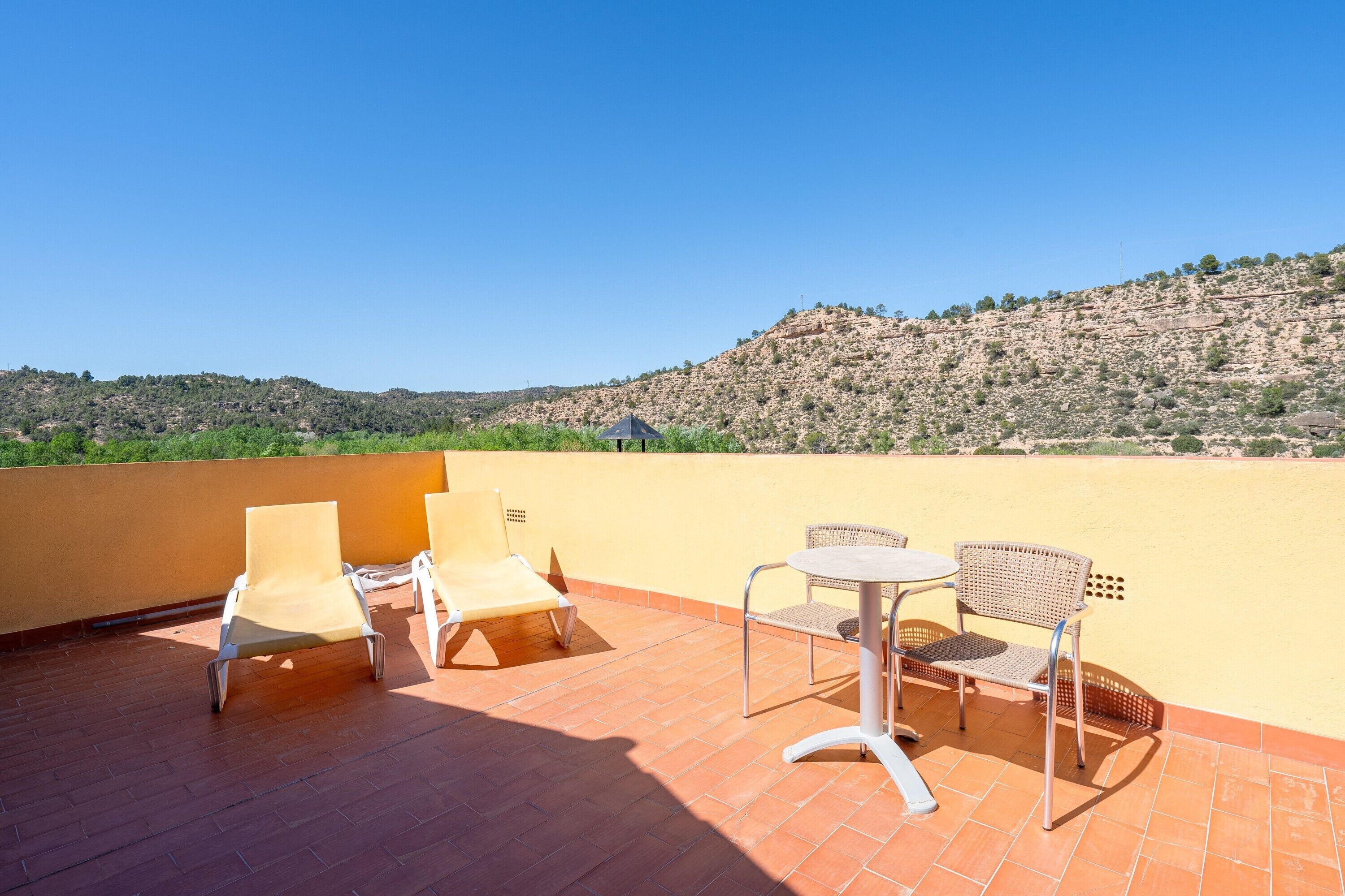 Terraço com cadeiras e uma mesa, com vista para uma paisagem montanhosa.