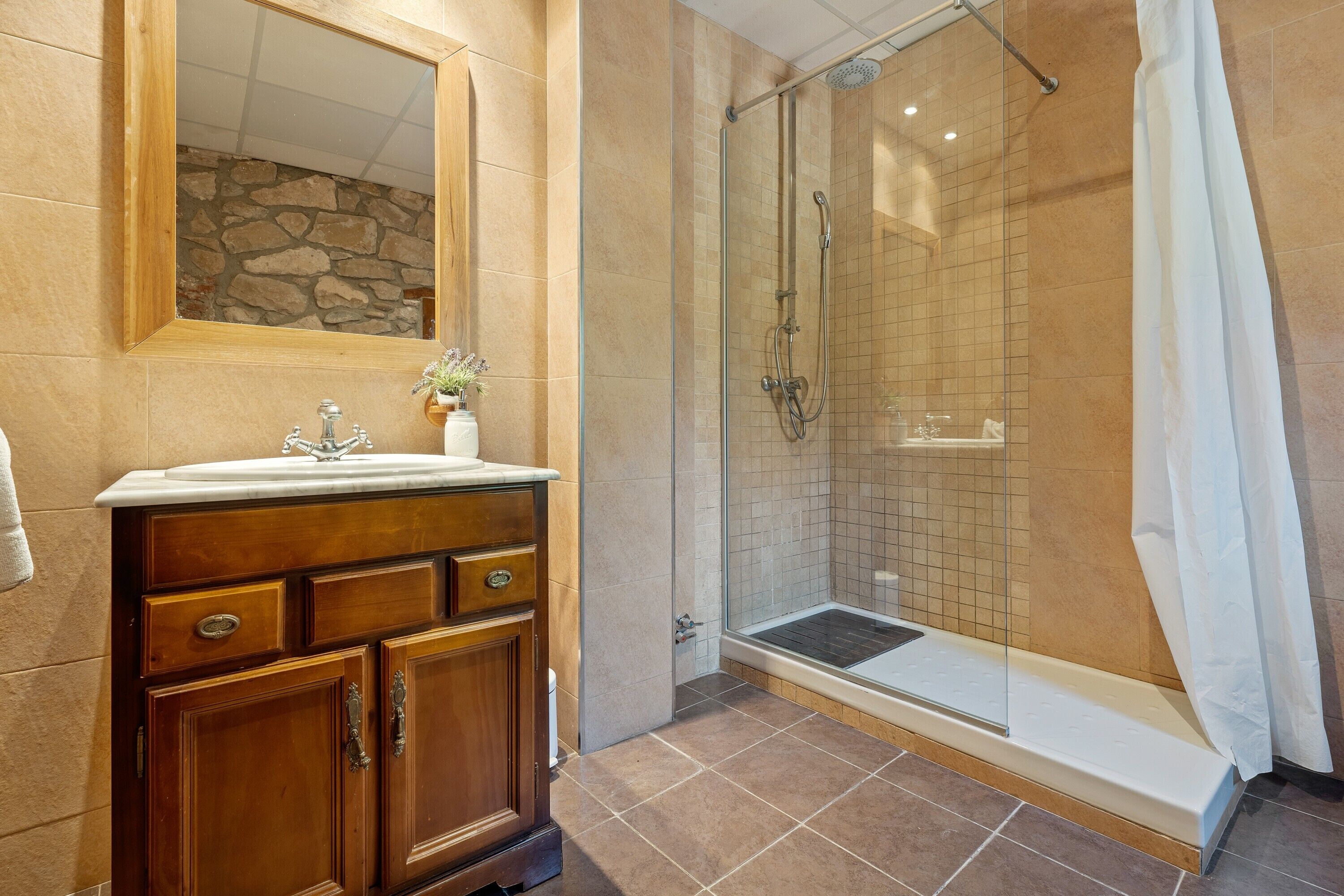 A bathroom with a wooden vanity, a glass shower enclosure, and a stone wall.