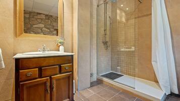 A bathroom with a wooden vanity, a glass shower enclosure, and a stone wall.