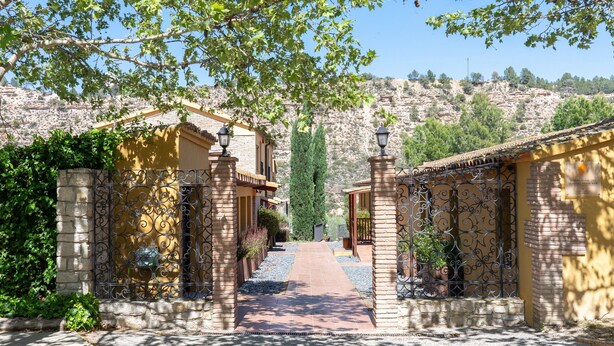 A courtyard with a paved walkway, a yellow building, and a stone wall.