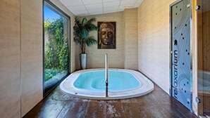 A hot tub in a room with a large window, a Buddha painting, and a potted plant.