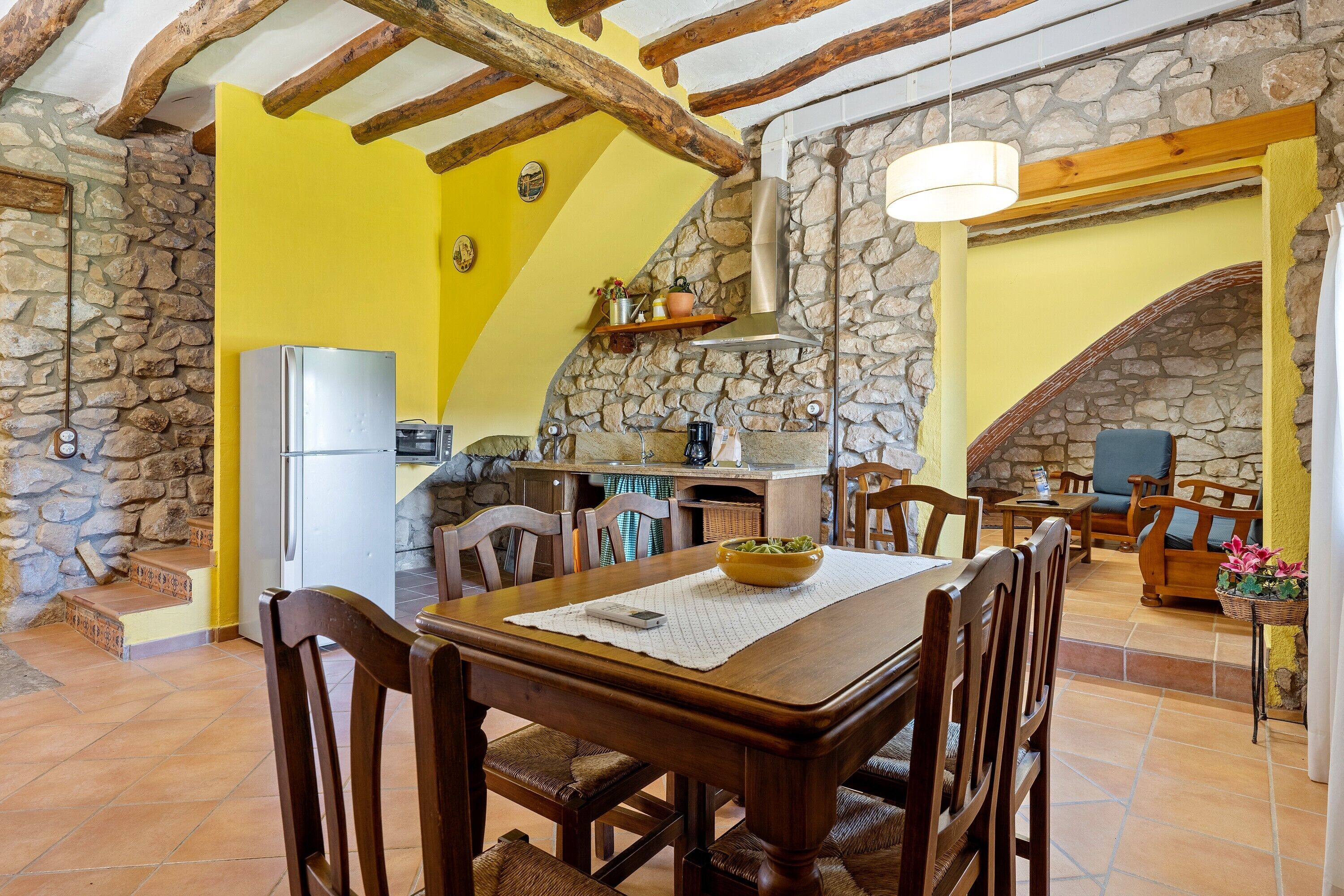 A dining area with a wooden table, chairs, a bowl, and a stone wall.