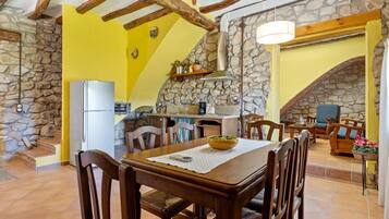 A dining area with a wooden table, chairs, a bowl, and a stone wall.