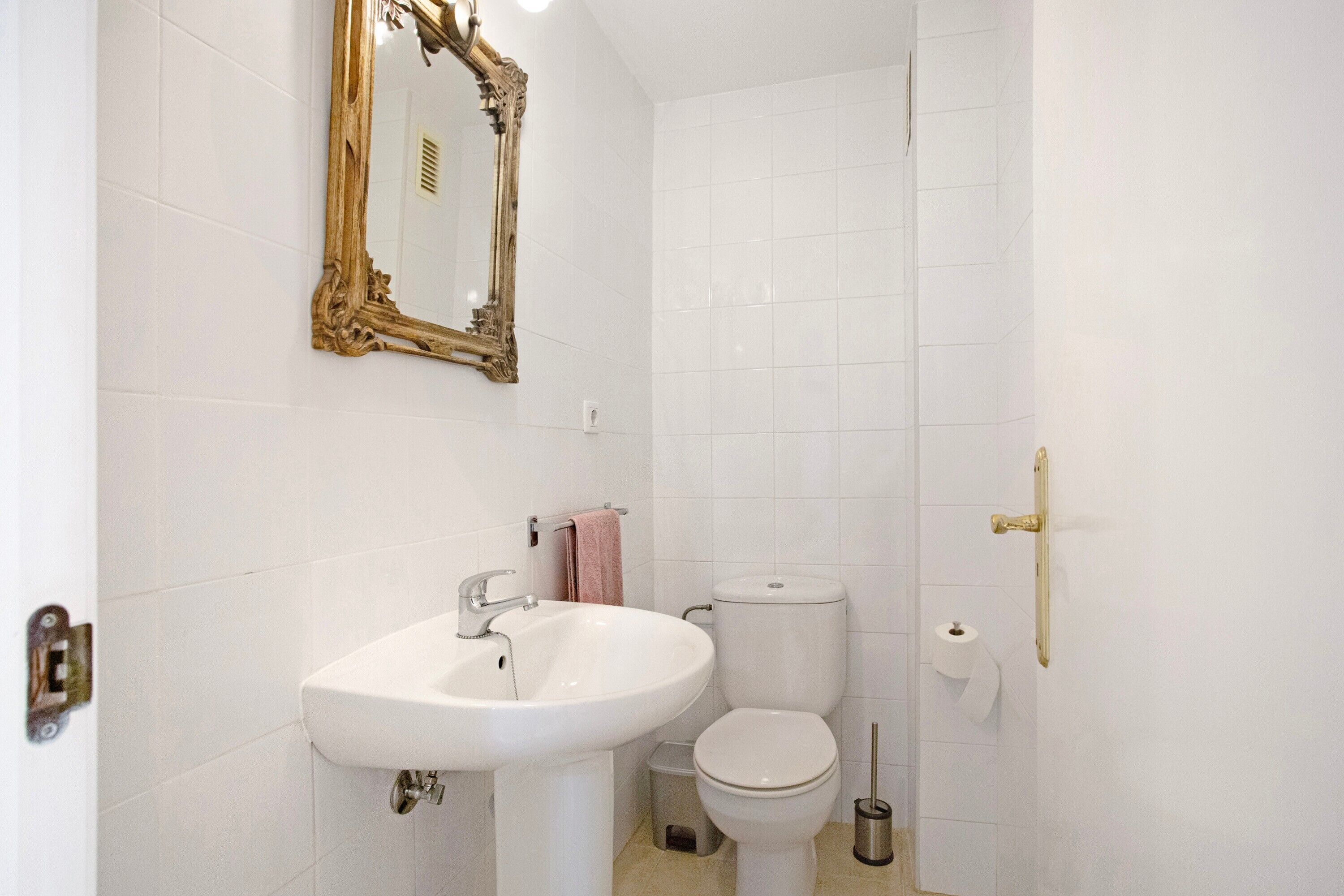 Et badeværelse med en hvid vask, toilet og et spejl med gylden ramme.