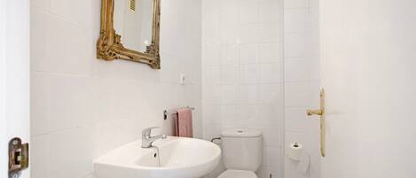 Et badeværelse med en hvid vask, toilet og et spejl med gylden ramme.