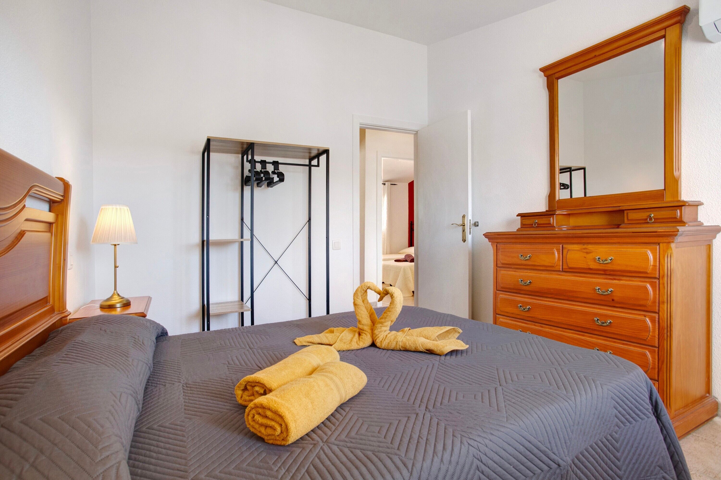 Een hotelkamer met een bed, een houten dressoir, een spiegel, een lamp en een kledingkast.