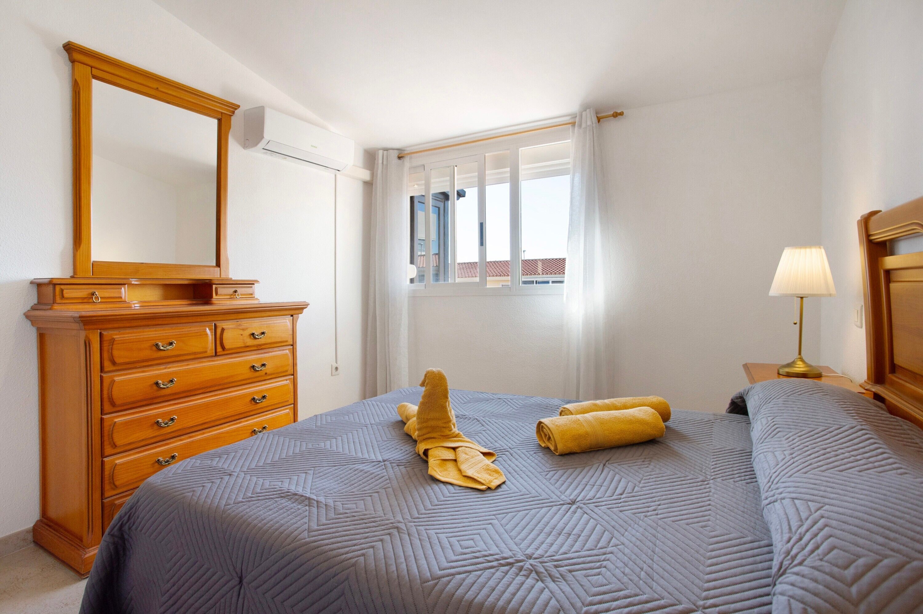 Una camera d'albergo con un letto, un comò di legno, una finestra con tende e una lampada.