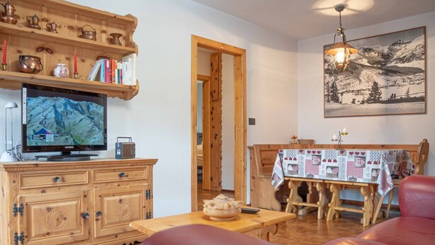 A cozy living room with a wooden cabinet, a television, and a dining table with a quilt-covered tablecloth. - Comfortable and spacious apartment for four people (Livigno)