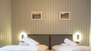 A hotel room with two beds, each with a neatly folded white towel. The room has wooden paneling on the walls and two framed pictures hanging above the beds. - Comfortable and spacious apartment for four people (Livigno)