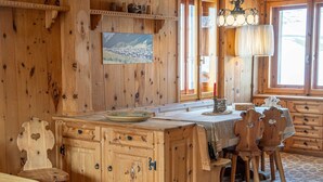A wooden cabin interior with a dining area, wooden cabinets, and a view through the window. - Typical wooden apartment, warm and cozy suitable for a large family (Livigno)