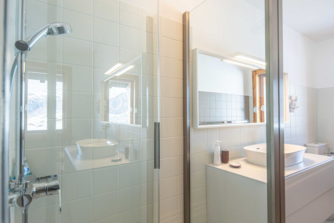 A modern bathroom with a glass shower enclosure, a white sink, and a large mirror.