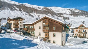A snow-covered mountain village with wooden buildings, including a hotel with balconies and a ski lift in the background. - Convenience, comfort and atmosphere at your fingertips (Livigno)