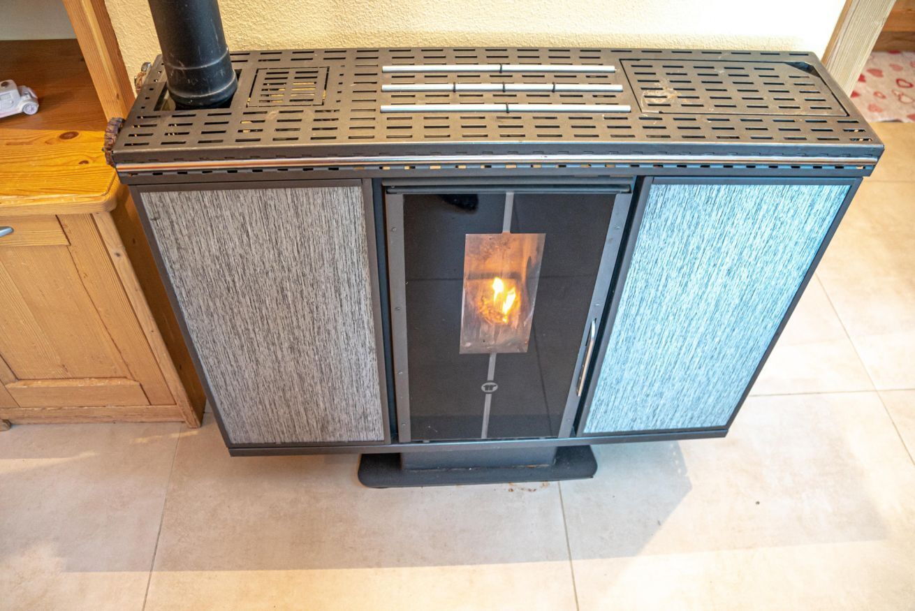A wood-burning stove with a glass door, a metal grate on top, and a black base.