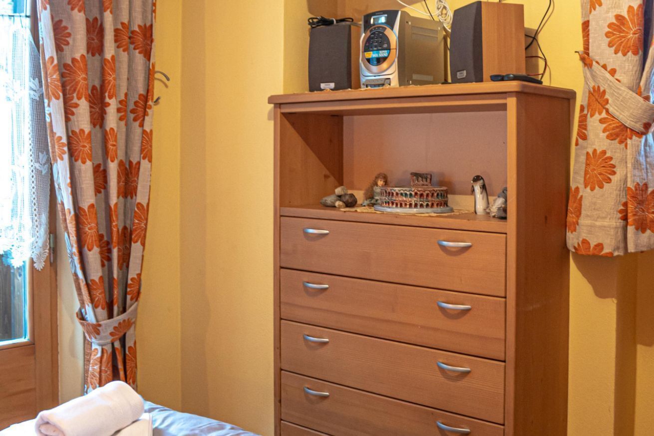 Une commode en bois avec des tiroirs, une petite étagère ornée d’objets décoratifs et une fenêtre avec des rideaux.